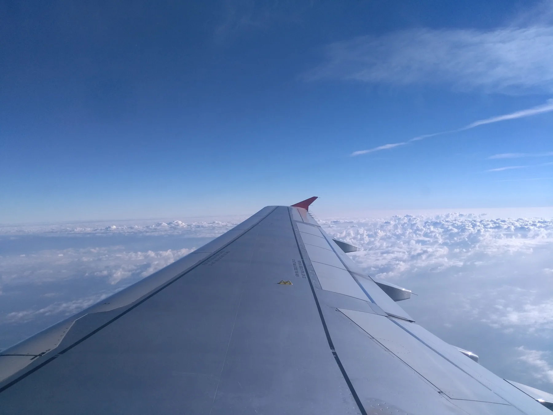 An aircraft wing above a broad layer of clouds under a blue sky
